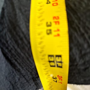 May include: A yellow measuring tape with black markings, showing measurements in feet and inches. The tape is positioned against a dark fabric, with measurements visible from 34 inches to 39 inches.
