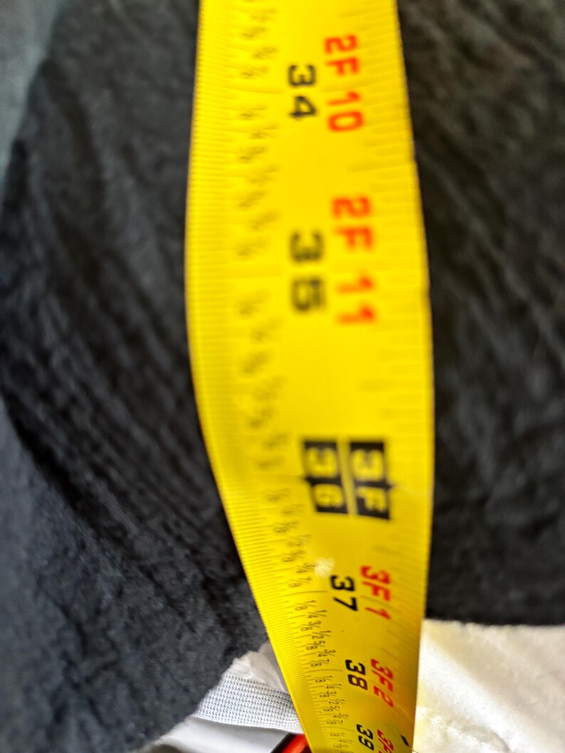 May include: A yellow measuring tape with black markings, showing measurements in feet and inches. The tape is positioned against a dark fabric, with measurements visible from 34 inches to 39 inches.