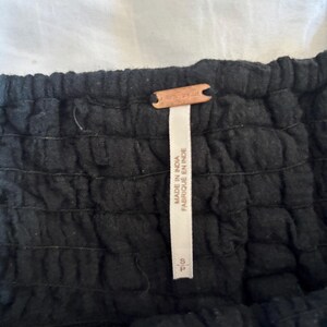May include: Close-up of a black garment with a textured, gathered design. A small, brown leather tag with the word "Free People" is attached. A white tag with text that reads "MADE IN INDIA FABRIQUE EN INDE" is also visible.