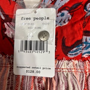 May include: Close-up of a red garment with a floral pattern and a tag. The tag reads "free people" and "RED ROME". The garment has a button and a barcode. The suggested retail price is $128.00.