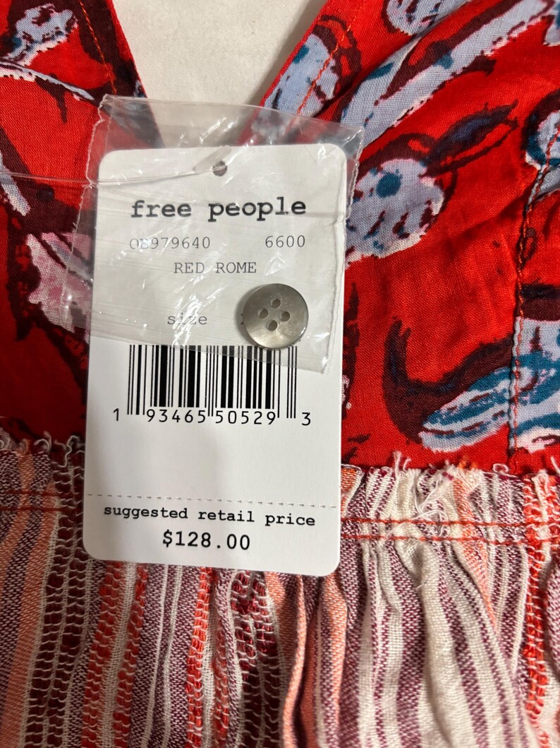 May include: Close-up of a red garment with a floral pattern and a tag. The tag reads "free people" and "RED ROME". The garment has a button and a barcode. The suggested retail price is $128.00.