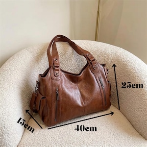 May include: A brown handbag with two top handles, featuring two vertical zippered pockets on the front and side pockets. The bag measures 40 cm in width, 25 cm in height, and 15 cm in depth, as indicated by the black measurement arrows on the image.