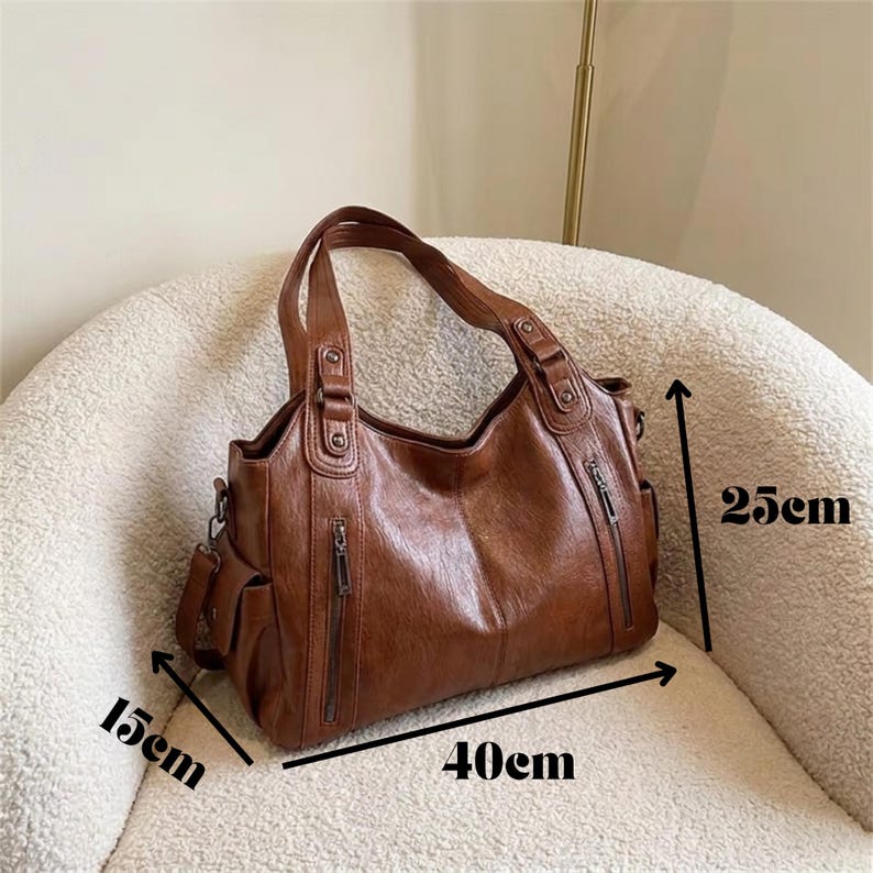 May include: A brown handbag with two top handles, featuring two vertical zippered pockets on the front and side pockets. The bag measures 40 cm in width, 25 cm in height, and 15 cm in depth, as indicated by the black measurement arrows on the image.