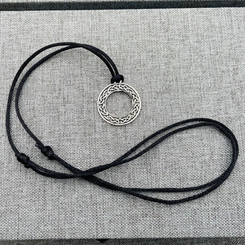 A silver Celtic knot pendant necklace with a black cord.