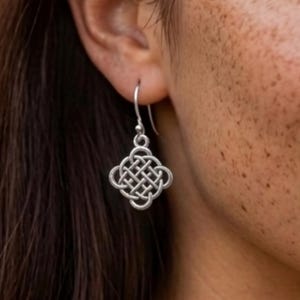 May include: A silver-toned earring featuring a square-shaped Celtic knot design with rounded corners. The pendant hangs from a simple curved metal hook. The intricate woven pattern consists of interconnected loops forming a symmetrical shape.
