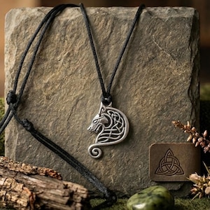 May include: A silver-toned metal pendant shaped like a stylized wolf head with intricate knotwork patterns, suspended from a thin black cord. The pendant features a curved tail design and is crafted with a metallic finish that highlights the detailed engravings.