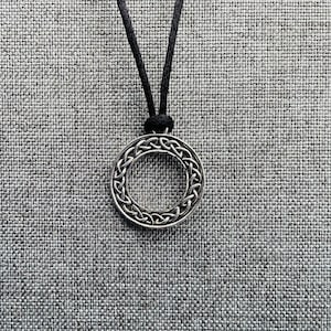A silver pendant necklace with a circular Celtic knot design. The pendant is hanging from a black cord.