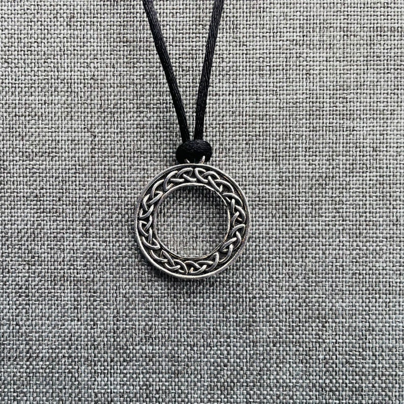 A silver pendant necklace with a circular Celtic knot design. The pendant is hanging from a black cord.