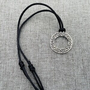 A silver Celtic knot pendant necklace with a circular design, hanging on a black cord.