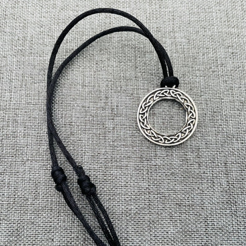 A silver Celtic knot pendant necklace with a circular design, hanging on a black cord.