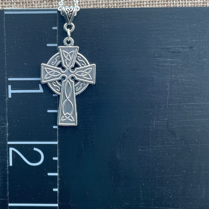A silver Celtic cross pendant with intricate knotwork designs. The pendant is hanging from a silver chain.