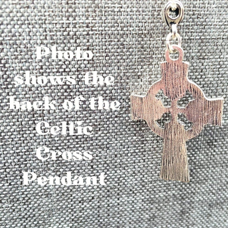 The back of a silver Celtic cross pendant. The pendant has a detailed design with intricate knots and a loop at the top for attaching a chain.