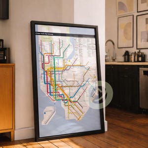 May include: A framed New York City Subway map, featuring a colorful network of subway lines. The map is in a black frame and leans against a white wall. The map includes the text "New York City Subway".