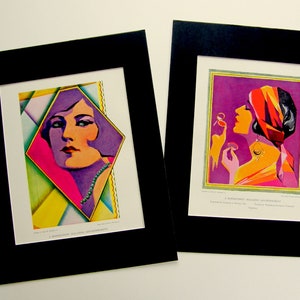 May include: Two framed vintage art prints featuring colorful illustrations of women in geometric designs. The first print features a woman with purple hair and a pink and yellow background. The second print features a woman with a red and orange turban and a purple background. Both prints have a black mat.