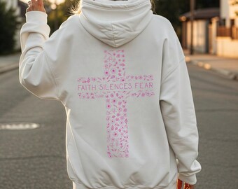 Könnte beinhalten: Ein weißer Kapuzenpullover mit einem floralen Kreuzdesign in Rosa auf dem Rücken, bestehend aus Blumen und Blättern. Der Text "FAITH SILENCES FEAR" ist auf dem Kreuz aufgedruckt. Der Hoodie hat eine Kapuze mit Kordelzug und lange Ärmel.