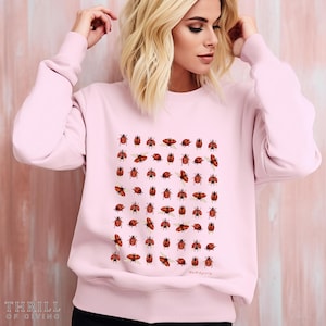 Puede incluir: Una sudadera rosa con un patrón de mariquitas rojas con alas doradas. La sudadera tiene cuello redondo y mangas largas. El texto "a world of giving" está impreso en la parte inferior del diseño.