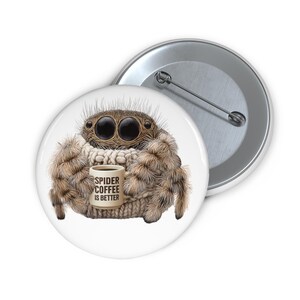 Op de afbeelding: Een witte button met een cartoon spin die een koffiemok vasthoudt. De spin is bruin en harig met grote ogen. Op de mok staat "SPIDER COFFEE IS BETTER". Een tweede, zilveren button is zichtbaar op de achtergrond.