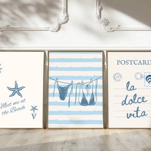 May include: Three framed art prints with beach-themed designs. One features a starfish and the text "Meet me at the Beach." Another shows a blue striped pattern with a bikini. The third says "Postcard la dolce vita."