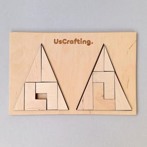 Puede incluir: Rompecabezas de madera con dos secciones triangulares, cada una con un rompecabezas geométrico. La base de madera tiene el texto "UsCrafting.". Las piezas del rompecabezas son de color marrón claro.