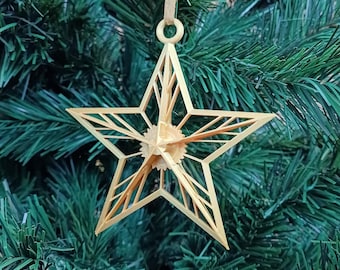 May include: A gold star-shaped Christmas bauble with a geometric design. The bauble is hanging from a green artificial Christmas tree.
