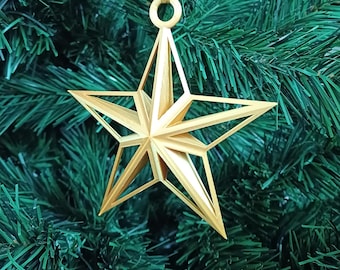 May include: A gold star-shaped Christmas bauble with a geometric design hangs from a green artificial Christmas tree.