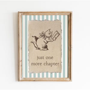 May include: Framed print featuring a whimsical illustration of a cat reading a book. The cat is drawn in brown ink on a textured background, with the text "just one more chapter" below. The frame is light brown, and the background has blue and white stripes.