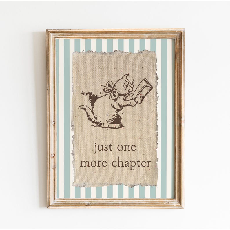 May include: Framed print featuring a whimsical illustration of a cat reading a book. The cat is drawn in brown ink on a textured background, with the text "just one more chapter" below. The frame is light brown, and the background has blue and white stripes.