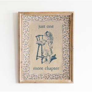 Pode incluir: Obra de arte emoldurada com uma ilustração vintage de uma menina lendo um livro. A imagem é em tons de azul, com o texto "just one more chapter". A moldura tem uma borda floral e um acabamento em madeira envelhecida.