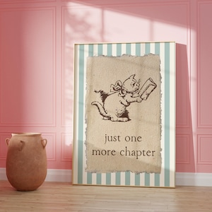 May include: A framed print featuring a whimsical illustration of a cat reading a book. The cat is brown and wearing a bow. The text "just one more chapter" is below the cat. The frame has a striped background with a light blue and white pattern.