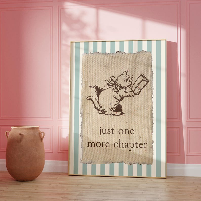 May include: A framed print featuring a whimsical illustration of a cat reading a book. The cat is brown and wearing a bow. The text "just one more chapter" is below the cat. The frame has a striped background with a light blue and white pattern.