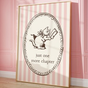 May include: A framed print with a cartoon cat reading a book inside an oval frame. The cat is brown, and the frame has a scalloped edge. The background is cream with pink and white vertical stripes. The text reads "just one more chapter."
