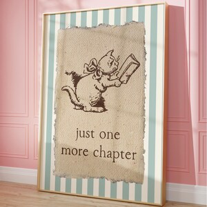 May include: A framed print featuring a brown illustration of a cat reading a book. The cat has a bow and is holding the book with both paws. The text "just one more chapter" is below the cat. The frame has a striped background.