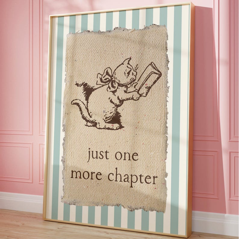 May include: A framed print featuring a brown illustration of a cat reading a book. The cat has a bow and is holding the book with both paws. The text "just one more chapter" is below the cat. The frame has a striped background.