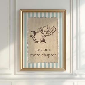 May include: Framed artwork featuring a sepia-toned illustration of a cat reading a book. The cat is wearing a bow and is set against a textured background with the words "just one more chapter". The frame has a gold finish.
