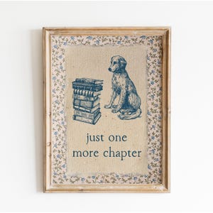 May include: A framed print featuring a blue illustration of a dog sitting next to a stack of books. The text "just one more chapter" is below the dog and books. The frame has a floral pattern.