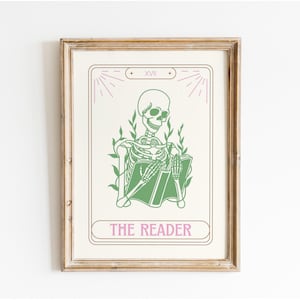Puede incluir: Una impresión enmarcada que presenta un esqueleto verde leyendo un libro, etiquetado como "THE READER". La obra de arte tiene una combinación de colores rosa claro y verde, con el número romano XVII en la parte superior. El marco es de color marrón claro.