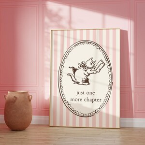 May include: A framed print with a charming illustration of a cat engrossed in a book, enclosed in an oval frame. The print is set against a striped backdrop and includes the text "just one more chapter". The frame has a gold finish.