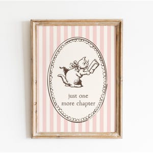 Op de afbeelding: Een ingelijste print met een illustratie van een kat die een boek leest. De kat staat in een ovale lijst met de tekst "just one more chapter". De achtergrond heeft roze en witte verticale strepen.