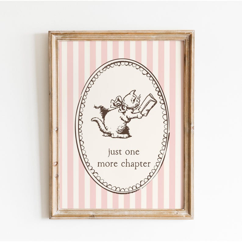 May include: Framed print with a cat illustration reading a book, set against a pink and white striped background. The oval frame contains the text "just one more chapter". The frame has a distressed, vintage look.