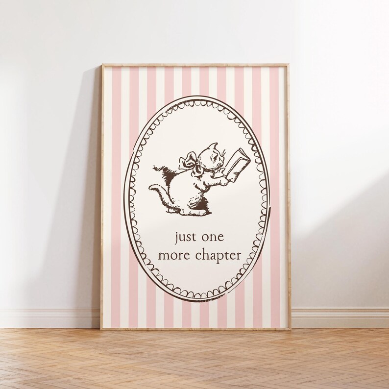 May include: A framed print with a brown illustration of a cat reading a book within an oval frame. The background has pink and white vertical stripes, and the text "just one more chapter" is below the cat.