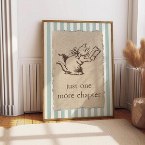 May include: Framed print featuring a sepia-toned illustration of a cat reading a book. The cat has a bow and is set against a textured background with the words "just one more chapter." The frame has a light blue and white striped border.