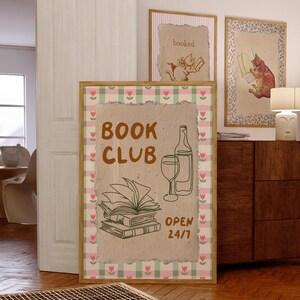 May include: A brown and white framed print with a gingham border. The print features a hand-drawn illustration of a stack of books, a glass of wine, and a bottle of wine. The text "BOOK CLUB OPEN 24/7" is printed on the print.