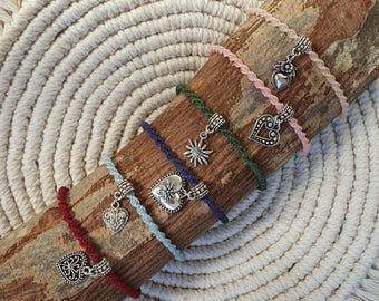 Könnte beinhalten: Fünf geflochtene Kordelarmbänder in Rot, Hellblau, Dunkelblau, Dunkelgrün und Hellrosa. Jedes Armband ist mit einem silberfarbenen Metallanhänger versehen, darunter Herzformen, ein Sonnenmotiv und ein Blumenmuster, befestigt mit einer Metallperle.