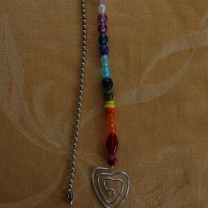 May include: A silver chain with a heart-shaped charm at the end. The chain is decorated with colorful beads in a rainbow pattern.