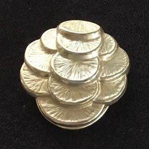 Può includere: Un fermaglio rotondo a forma di fiore, decorativo, color argento con una superficie testurizzata.