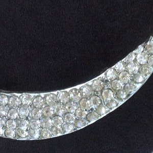 Op de afbeelding: Een zilverkleurige broche in de vorm van een halve maan, bezet met heldere strass steentjes.