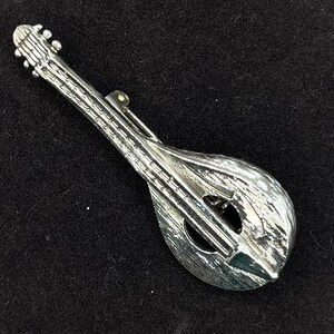 May include: A silver-toned metal brooch in the shape of a mandolin.