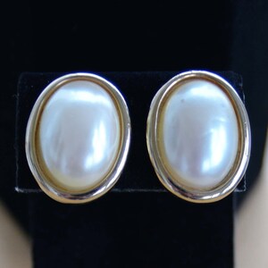 Puede incluir: Un par de pendientes de tono dorado con acentos de perlas blancas ovaladas.