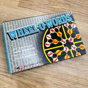 May include: A board game called "Wheel O-Words" with a black and yellow circular game board featuring the letters F, I, N, D, U, A, B, E, O, and T. The game board is surrounded by a black border with white lettering.