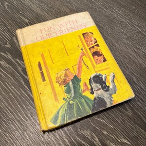 Könnte beinhalten: Ein gebundenes Vintage-Buch mit dem Titel Fun With Our Friends und einem leuchtend gelben Einband, der ein Kind in einem grünen Kleid zeigt, das nach einer Türklinke greift, sowie einen Hund und zwei Kinder, die aus einem Fenster schauen.